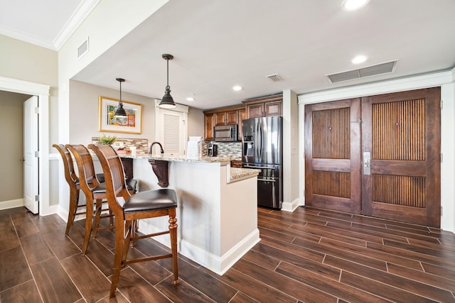kitchen with appliances with stainless steel finishes, a peninsula, crown molding, dark wood-style flooring, and light stone counters