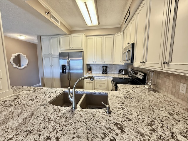 kitchen with a textured ceiling, decorative backsplash, a sink, appliances with stainless steel finishes, and light stone countertops