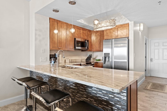 kitchen with light stone countertops, a peninsula, a sink, stainless steel appliances, and baseboards