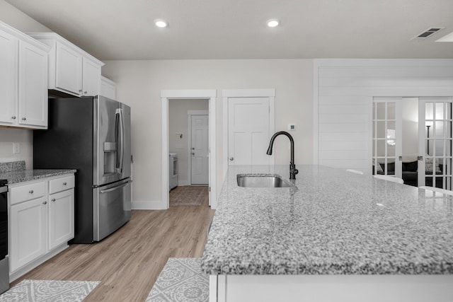 kitchen featuring a sink, stainless steel fridge, white cabinets, washer / dryer, and light stone counters