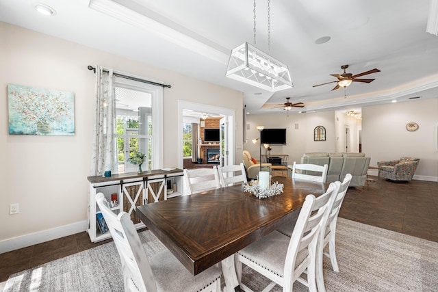 135 Bayou Point Dr, Santa Rosa Beach, FL 32459 - dining area featuring a ceiling fan, a warm lit fireplace, a tray ceiling, baseboards, and tile patterned flooring