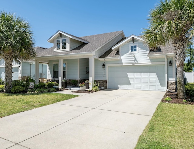 view of front of property featuring a front lawn, driveway, stone siding, covered porch, and an attached garage