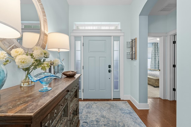foyer with arched walkways, a healthy amount of sunlight, visible vents, baseboards, and dark wood-style floors