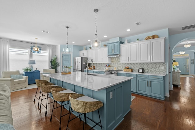 kitchen featuring arched walkways, visible vents, freestanding refrigerator, a kitchen bar, and decorative backsplash