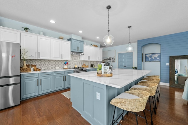 kitchen featuring a center island with sink, dark wood-style flooring, backsplash, decorative light fixtures, and appliances with stainless steel finishes