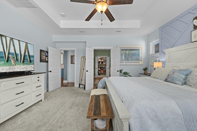 bedroom with a raised ceiling, visible vents, a walk in closet, light colored carpet, and ceiling fan