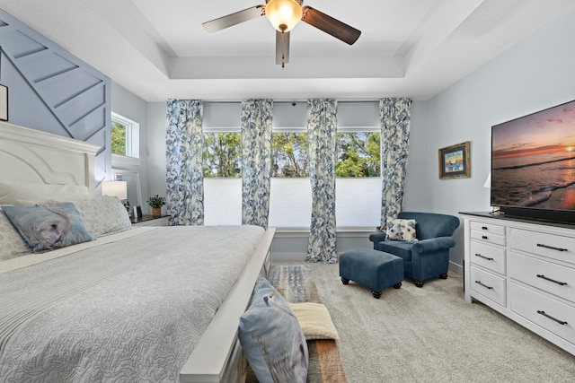 bedroom featuring a tray ceiling, light colored carpet, and ceiling fan