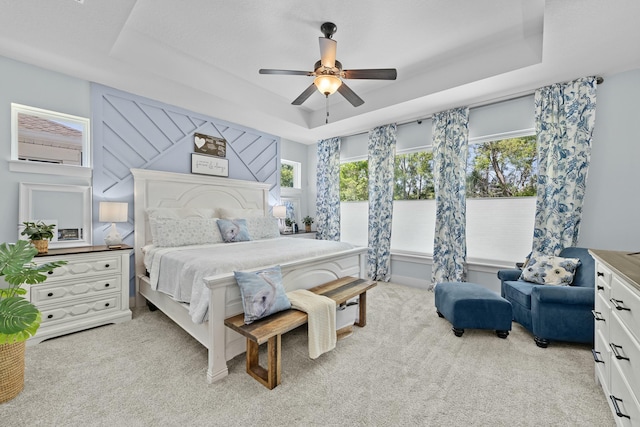 bedroom with light carpet, a ceiling fan, and a raised ceiling
