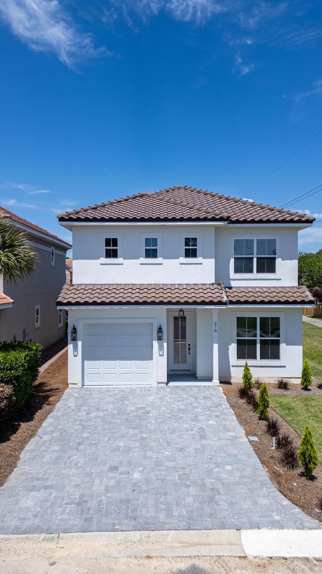 mediterranean / spanish house featuring stucco siding, an attached garage, decorative driveway, and a tile roof