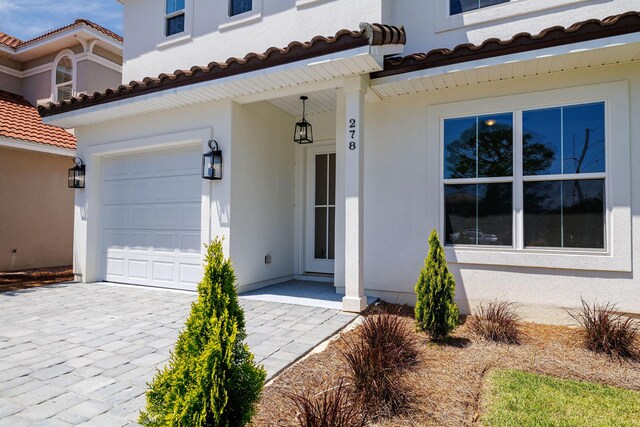 view of exterior entry with stucco siding, decorative driveway, a tiled roof, and a garage