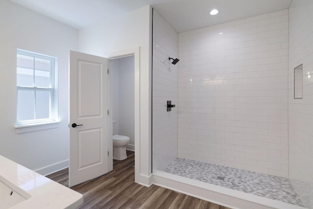 full bath featuring wood finished floors, baseboards, a tile shower, toilet, and recessed lighting