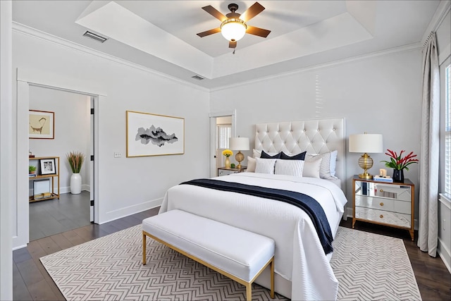 bedroom featuring dark wood-type flooring, visible vents, baseboards, and a tray ceiling
