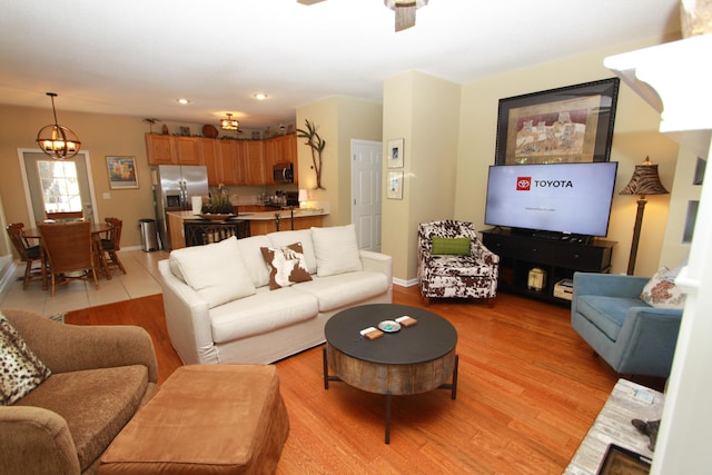 living room featuring baseboards, recessed lighting, light wood finished floors, and ceiling fan with notable chandelier