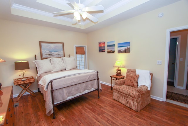 bedroom featuring ornamental molding, wood finished floors, baseboards, a tray ceiling, and a ceiling fan