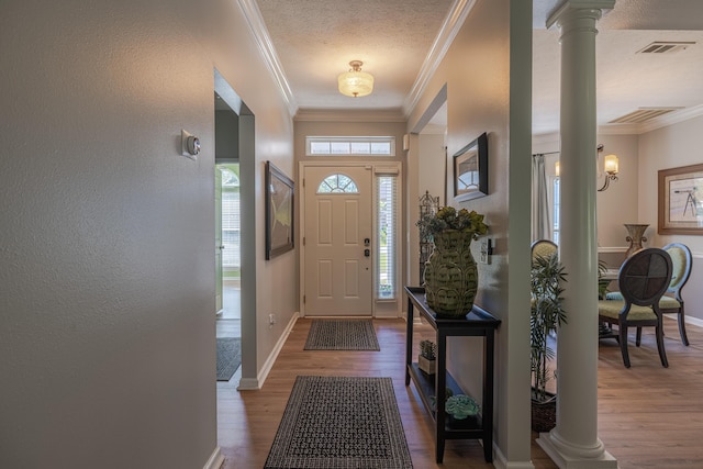 foyer with baseboards, ornate columns, wood finished floors, a textured wall, and ornamental molding