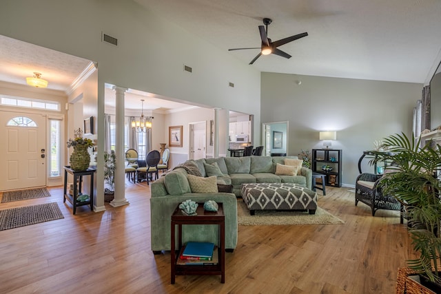 living room featuring visible vents, ornate columns, ceiling fan with notable chandelier, high vaulted ceiling, and ornamental molding