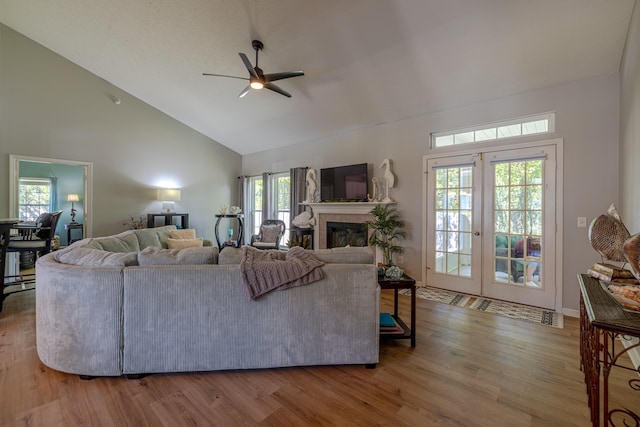 living area with high vaulted ceiling, a ceiling fan, a glass covered fireplace, and wood finished floors