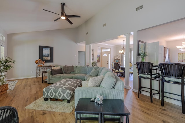 living area with visible vents, light wood-type flooring, decorative columns, high vaulted ceiling, and ceiling fan with notable chandelier