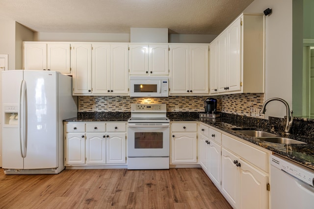 kitchen with dark stone counters, light wood finished floors, a sink, and white appliances