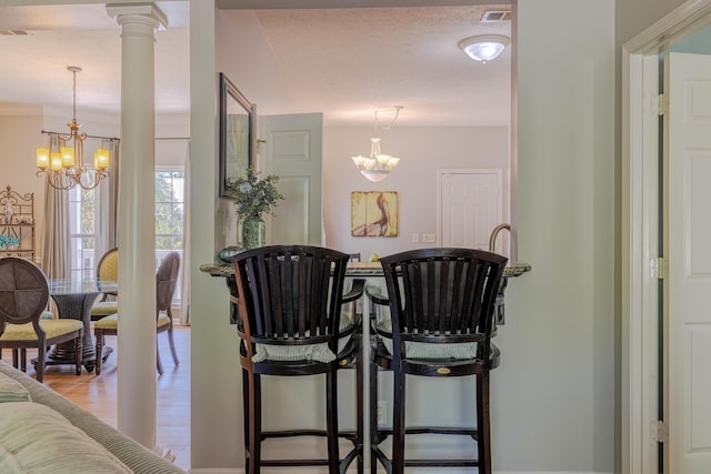 dining room with wood finished floors, visible vents, a chandelier, and ornate columns