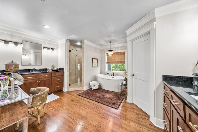 bathroom featuring a freestanding tub, wood finished floors, a shower stall, vanity, and ornamental molding
