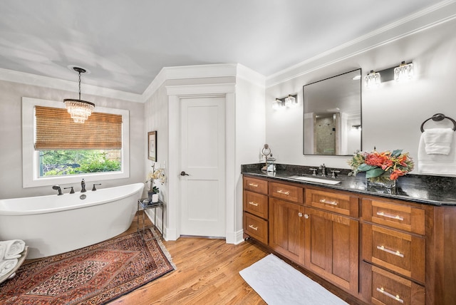 full bathroom featuring wood finished floors, vanity, crown molding, a soaking tub, and a notable chandelier