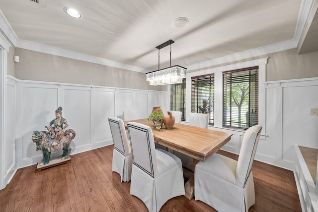 dining space with wainscoting, a chandelier, ornamental molding, and a decorative wall