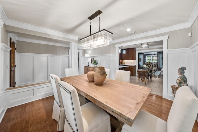 dining room with dark wood-style flooring, decorative columns, a notable chandelier, crown molding, and a decorative wall