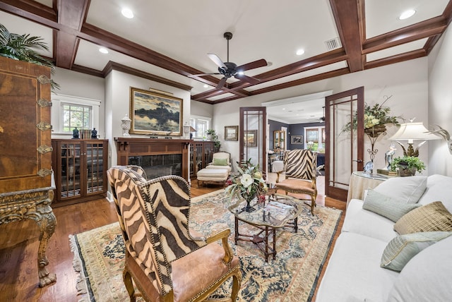 living area with coffered ceiling, wood finished floors, ornamental molding, beam ceiling, and ceiling fan