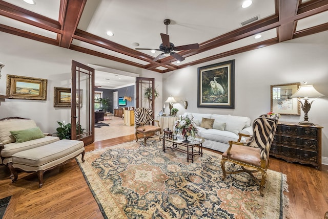 living area with visible vents, coffered ceiling, a ceiling fan, wood finished floors, and crown molding