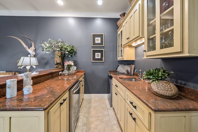 kitchen with a sink, crown molding, baseboards, glass insert cabinets, and cream cabinets