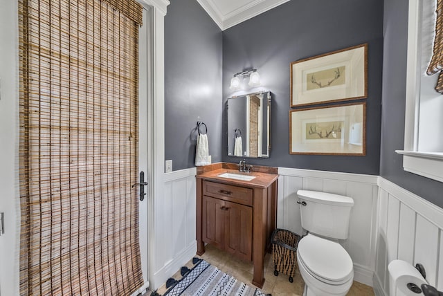 bathroom with a wainscoted wall, toilet, vanity, a decorative wall, and crown molding