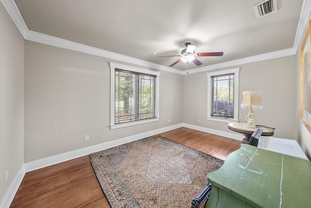 interior space with wood finished floors, visible vents, a ceiling fan, ornamental molding, and baseboards