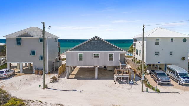 rear view of property featuring a water view, a carport, driveway, a shingled roof, and stairs