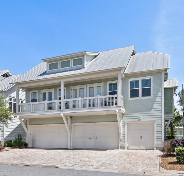 view of front of house with decorative driveway, metal roof, a balcony, and an attached garage