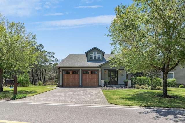view of front of house featuring a shingled roof, a front yard, decorative driveway, and a garage