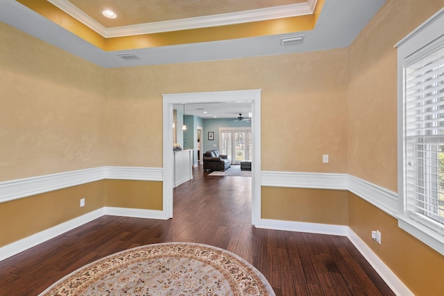interior space featuring wood finished floors, a tray ceiling, baseboards, ornamental molding, and visible vents