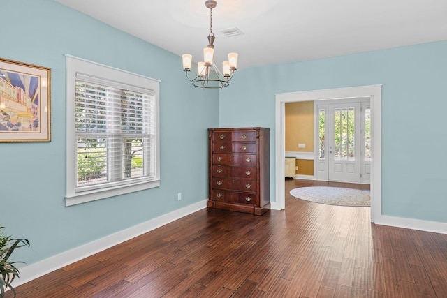 empty room featuring dark wood finished floors, visible vents, baseboards, and a notable chandelier