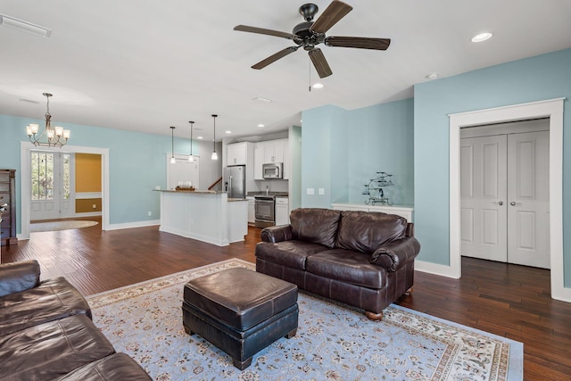 living area with baseboards, dark wood-style flooring, and ceiling fan with notable chandelier