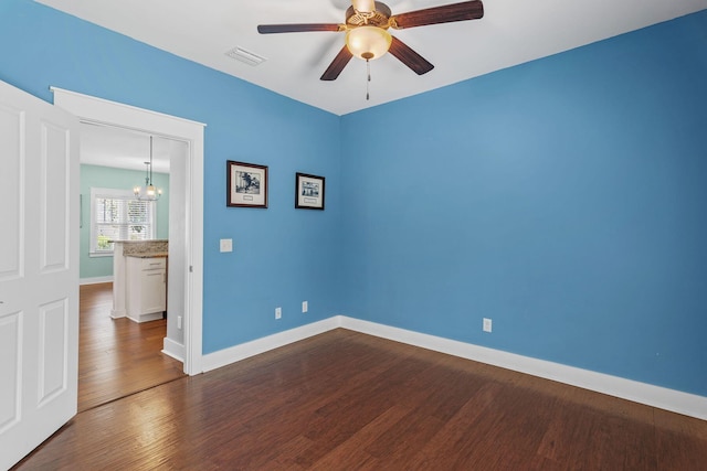 unfurnished room featuring baseboards, dark wood-style flooring, visible vents, and ceiling fan with notable chandelier