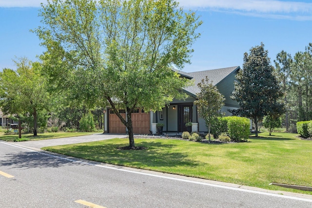 view of property hidden behind natural elements with driveway, a front yard, and a garage