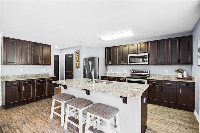 3129 Partridge Dr, Crestview, FL 32539 - kitchen with appliances with stainless steel finishes, light wood finished floors, a kitchen bar, dark brown cabinetry, and a center island with sink