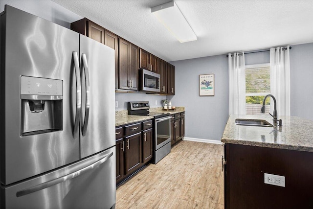 3129 Partridge Dr, Crestview, FL 32539 - kitchen featuring stainless steel appliances, a sink, light wood-style floors, dark brown cabinetry, and light stone counters