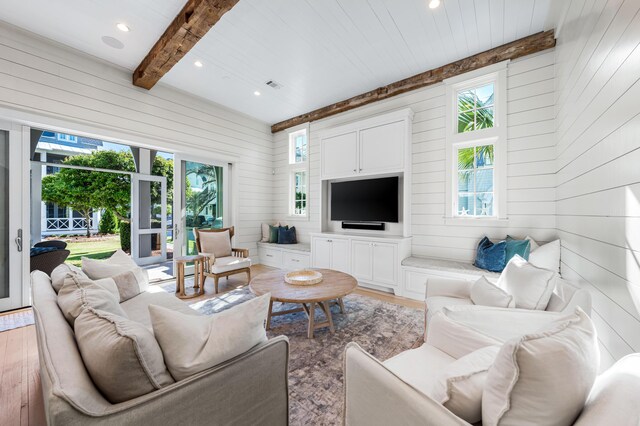 living room with beam ceiling, a wealth of natural light, wooden walls, and light wood-type flooring