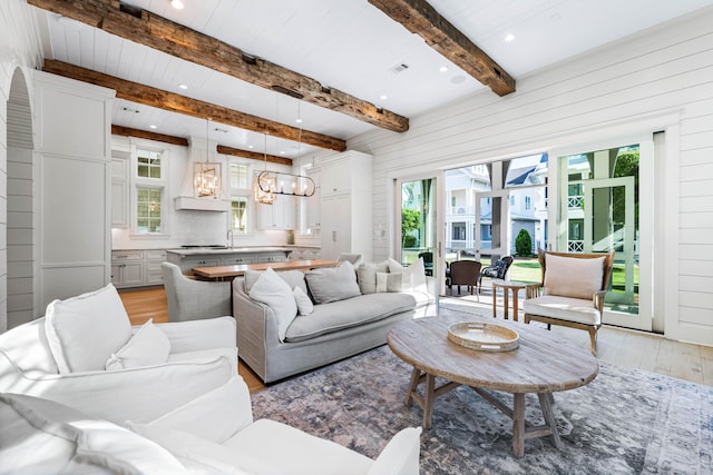 living room with beam ceiling, wooden walls, recessed lighting, light wood finished floors, and a notable chandelier