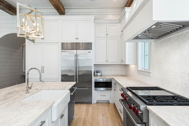kitchen with white cabinetry, a sink, high quality appliances, custom exhaust hood, and a notable chandelier