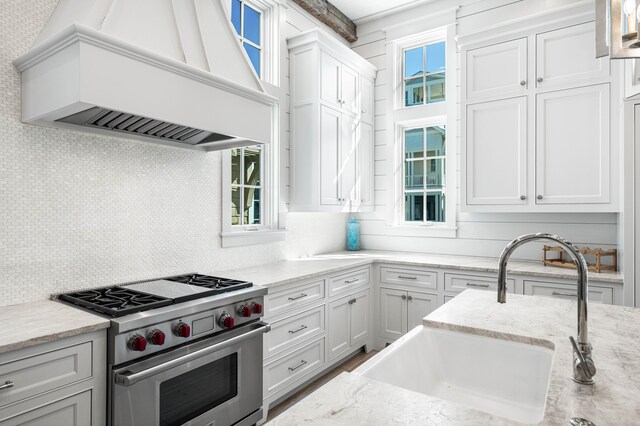 kitchen with a sink, decorative backsplash, custom range hood, luxury stove, and white cabinets