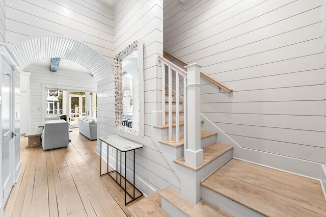 stairs featuring hardwood / wood-style floors, wood walls, and arched walkways