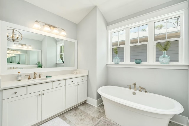 full bath featuring baseboards, an inviting chandelier, vanity, and a soaking tub