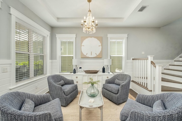 living area with an inviting chandelier, a raised ceiling, a wainscoted wall, and visible vents